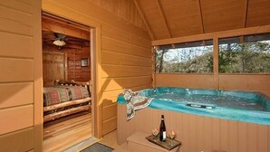 A wooden cabin with a hot tub, a bed with a blanket, and a wicker basket. - Misty Mornings: Rustic Resort Cabin - Pet Friendly - New Hot Tub (Sevierville)