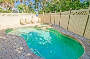 Piscina com borda de tijolos, cercada por uma cerca de madeira e um pequeno deck com cadeiras e guarda-sol.