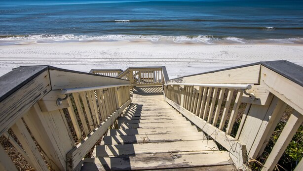 Une promenade en bois qui mène à une plage offrant une vue dégagée sur l’océan.