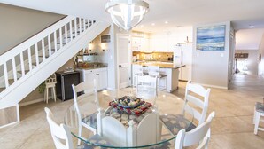 Une cuisine moderne avec des meubles blancs, un îlot central et un coin repas comprenant une table en verre et des chaises blanches.