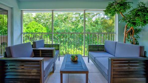 Un balcone con due divani, un tavolo e vista su una vegetazione rigogliosa.