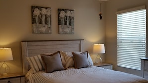 A bedroom with a large bed, two bedside tables with lamps, a headboard, and two wall-mounted paintings. - Walk to Lake Sumter Landing! Golf cart included! (The Villages)