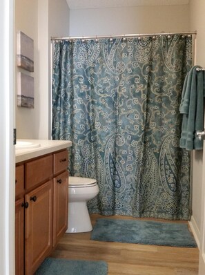 Un bagno con il water, mobili in legno, un lavandino e una tenda da doccia con un motivo paisley.
