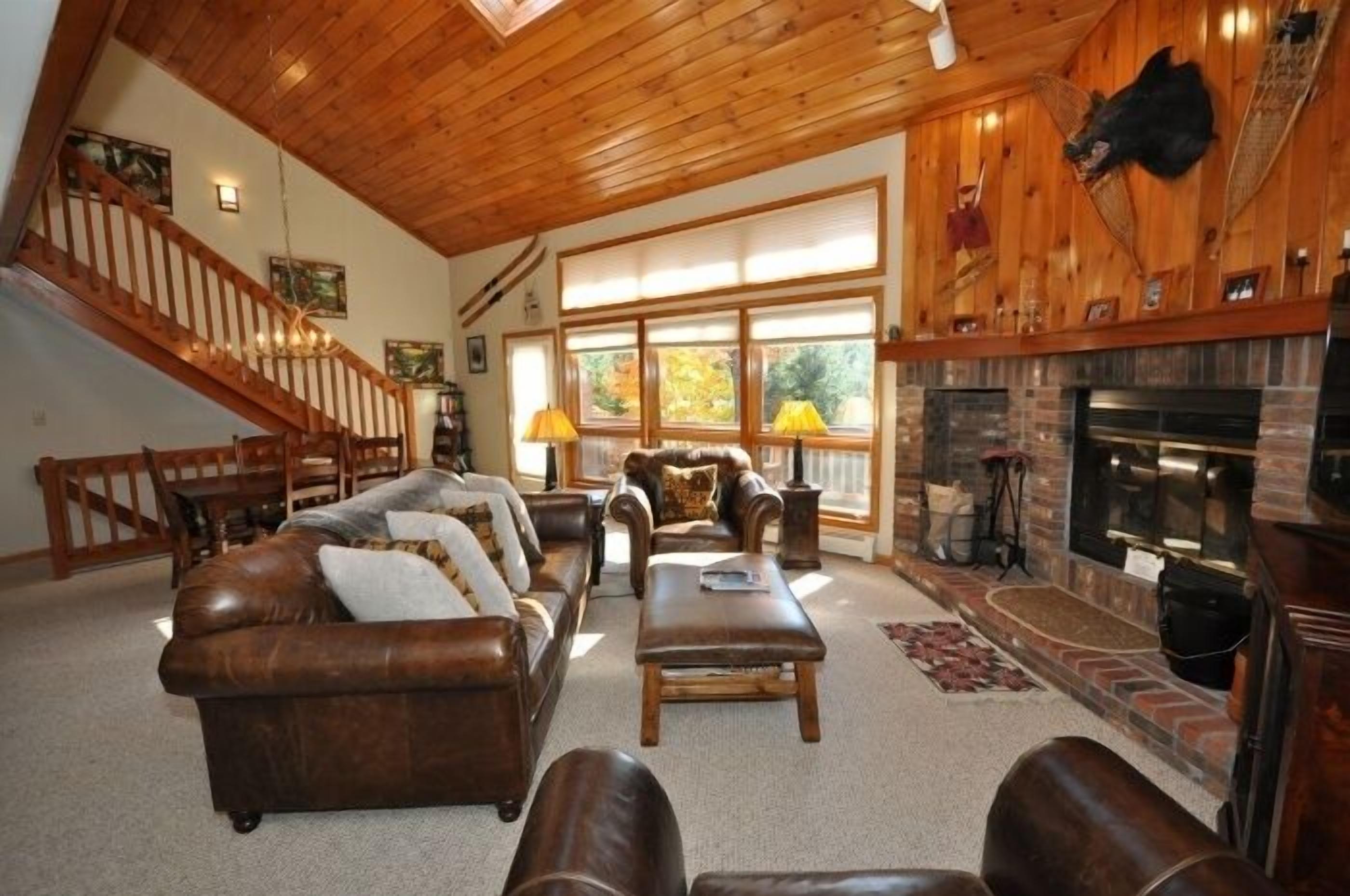 A spacious living room with a fireplace, leather sofas, and a staircase.