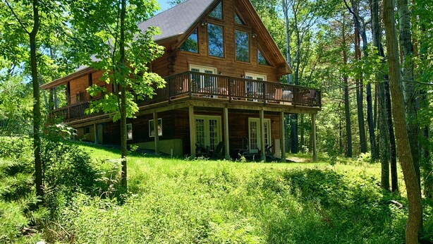 A log cabin with a balcony, surrounded by lush greenery and tall trees.