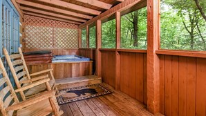 Eine Holzhütte mit Whirlpool, Holzbanken und Blick auf den Wald.