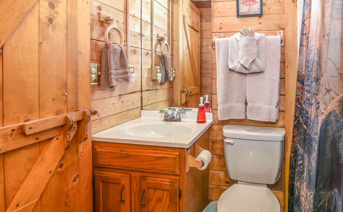 A wooden cabin bathroom with a sink, toilet, and towels hanging on the wall.