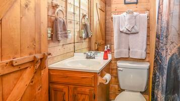 A wooden cabin bathroom with a sink, toilet, and towels hanging on the wall.