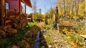 A rustic cabin with a wooden porch, a small stream, and a garden area with autumn foliage. - Beautiful cabin in aspen forest, amazing deck, lake and mountain views, private (Grand Lake)