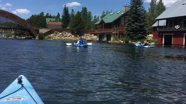 A calm river with kayaks, a wooden bridge, and a lodge with a green roof. - Beautiful cabin in aspen forest, amazing deck, lake and mountain views, private (Grand Lake)