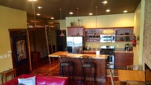 A spacious living area with a red sofa, a wooden dining table, and a kitchen area with a refrigerator, stove, and bar stools. - The Nest: Beautiful Apartment Style Lodging In The Heart Of Downtown Decorah. (Decorah)