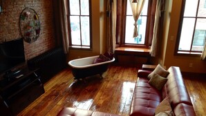 A living room with a red leather sofa, a vintage bathtub, a television, and a brick wall. - The Nest: Beautiful Apartment Style Lodging In The Heart Of Downtown Decorah. (Decorah)