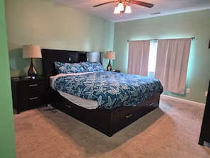 A bedroom with a bed, two bedside tables, a ceiling fan, and a window with curtains.