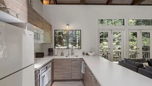 Eine moderne Küche mit einer großen Kochinsel, Holzschränken und Blick ins Freie durch große Fenster.