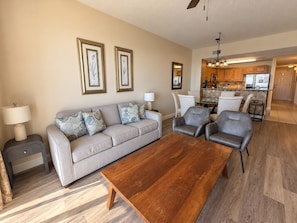 A living room with a sofa, two armchairs, a coffee table, and a kitchen in the background.