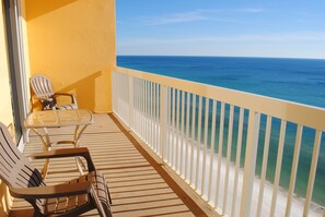 Un balcón con dos sillas y una mesa, con vistas a una playa y agua azul cristalina.