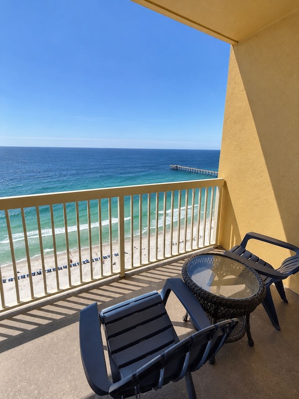 A balcony with a view of the ocean and a pier. There are two chairs and a table.