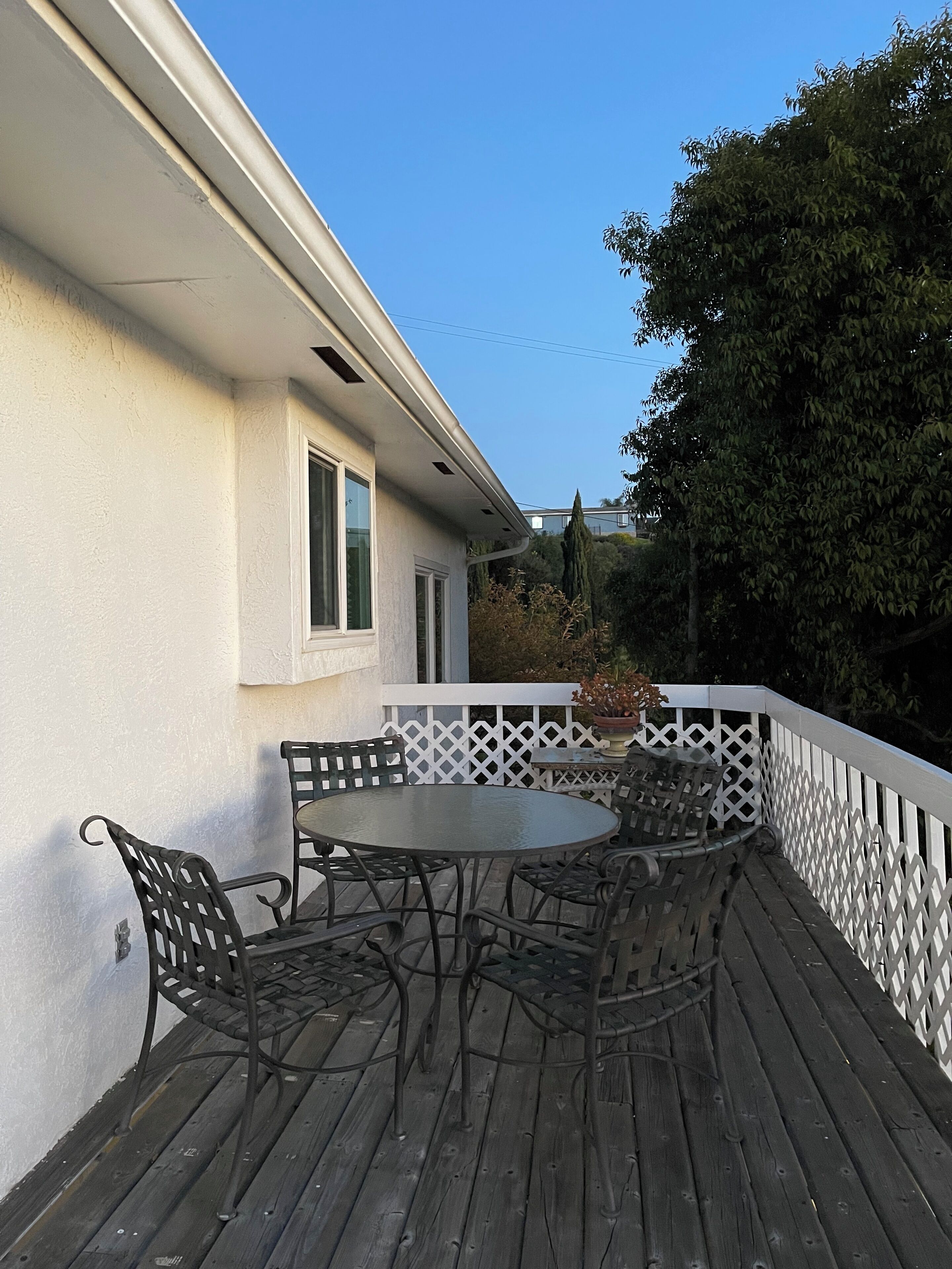 Un patio in legno con un tavolo rotondo e sedie, circondato da un recinto a graticcio bianco.