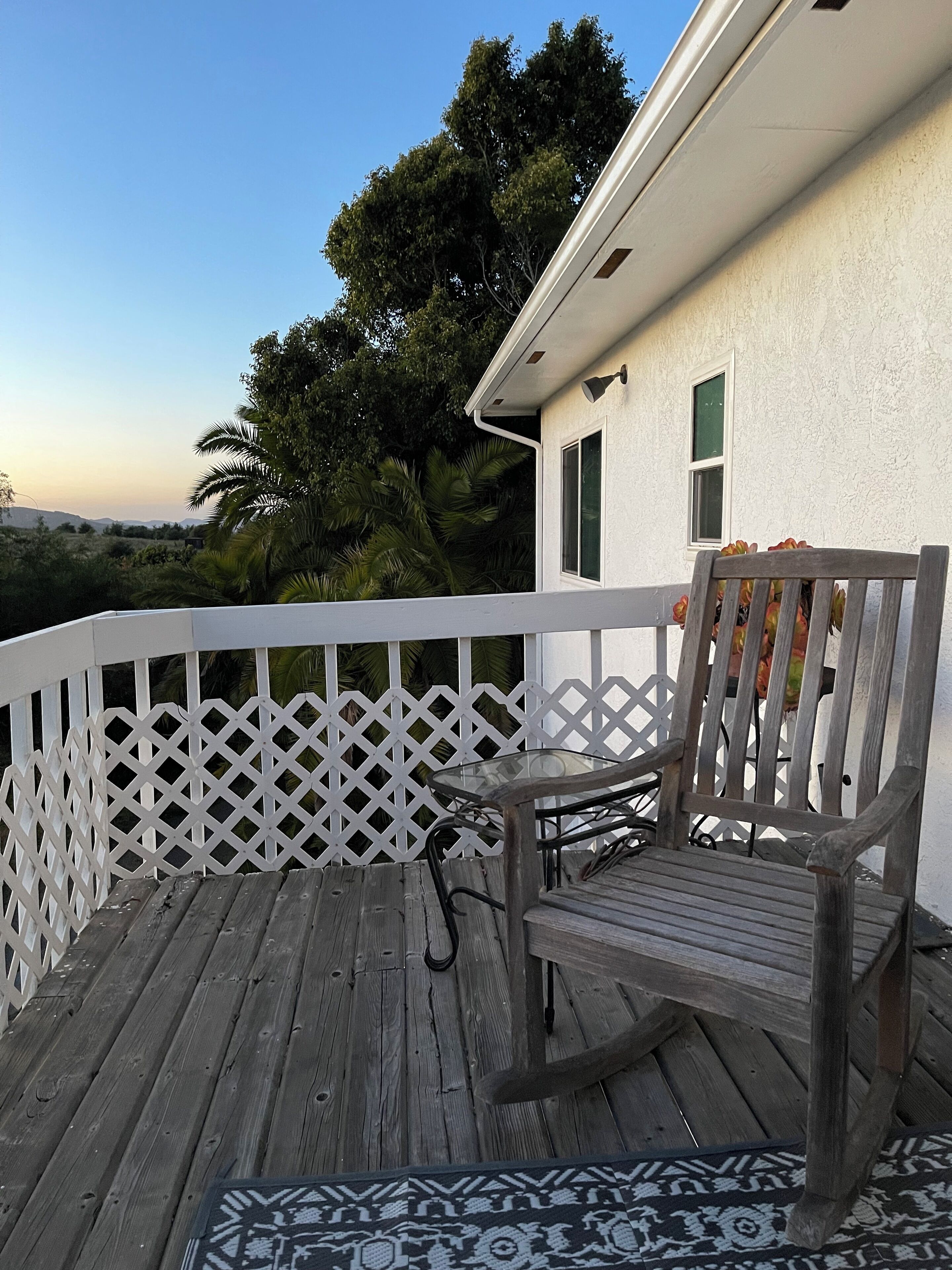 A wooden deck with a white lattice railing, a wooden chair, and a glass table.