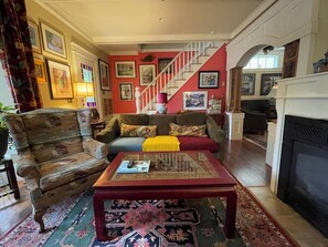 A living room with a sofa, armchair, coffee table, and a staircase. - In the Heart of Maine, Nestled in Camden Village (Camden)