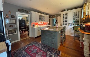 A spacious kitchen with a central island, wooden flooring, and a red patterned rug. - In the Heart of Maine, Nestled in Camden Village (Camden)