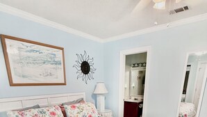 A bedroom with a bed, a nightstand, a lamp, a mirror, and a door leading to a bathroom.