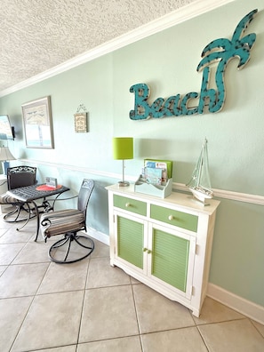 Una stanza con una parete verde, una scrivania, una sedia, un armadio e un cartello decorativo con la scritta 'Beach'.