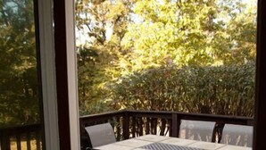 Une terrasse avec une table et des chaises, entourée d’une plateforme en bois et d’une haie.