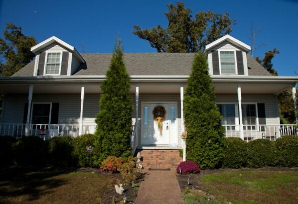 A two-story house with a front porch, a brick entrance, and a small garden with various plants. - Great for Family Reunions, Hunting Lodge And Pet Friendly! (Crofton)