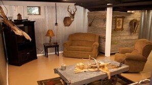 Un salon avec un fauteuil marron, une table basse en bois ornée de bois de cerf, une lampe et une tête de cerf accrochée au mur.