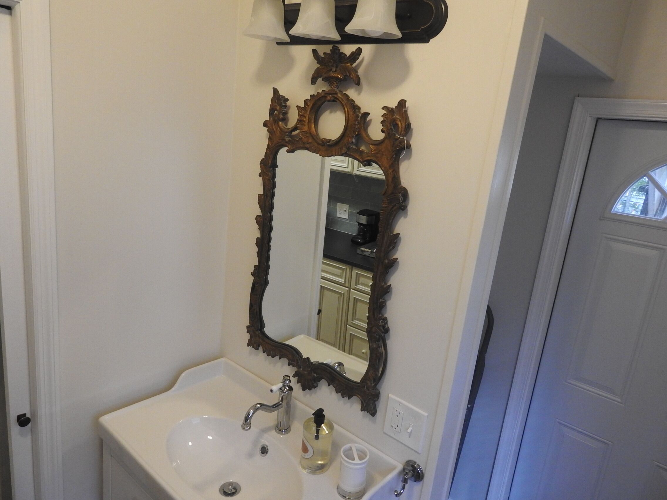 A bathroom with a white sink, a mirror with an ornate frame, and a light fixture above the mirror.