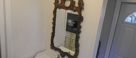 A bathroom with a white sink, a mirror with an ornate frame, and a light fixture above the mirror.