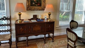 Une console en bois, ornée de deux lampes, d’un tableau floral encadré et d’un panneau indiquant l’emplacement du livre d’or.