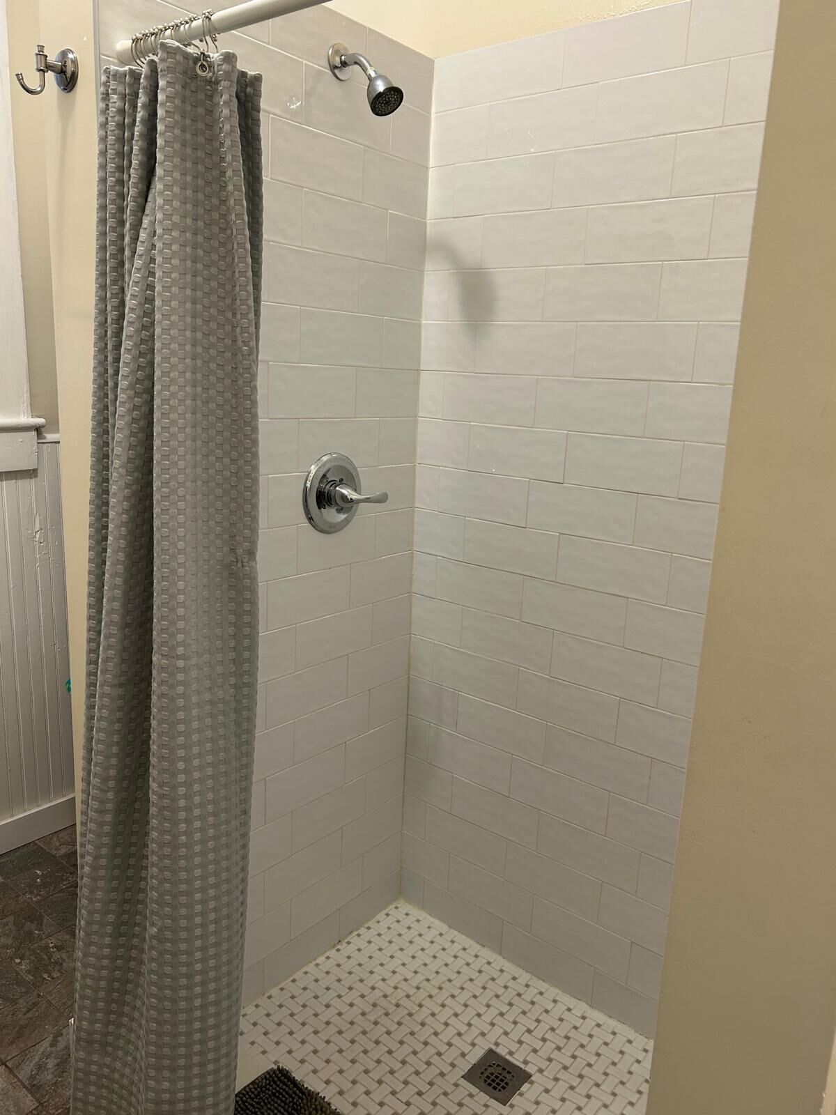 Une douche avec une porte en verre, des murs recouverts de carreaux blancs et une pomme de douche fixée au mur.