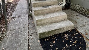 Une porte d’entrée avec un petit porche et un escalier en béton menant à la porte.