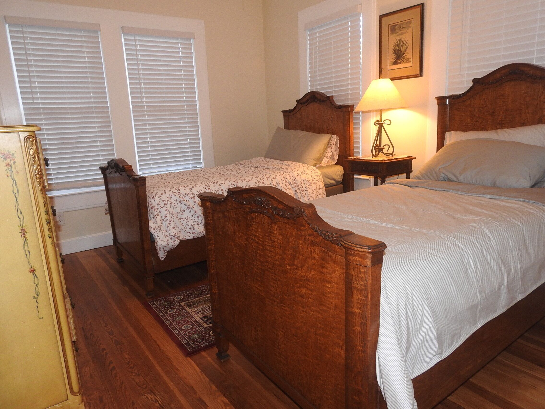 A bedroom with two wooden beds, a nightstand with a lamp, a dresser, and a window with blinds.