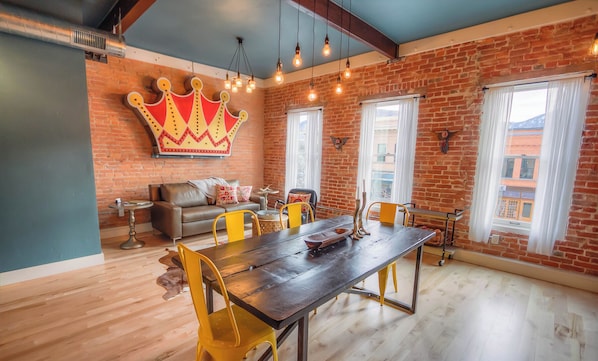 Un comedor con una larga mesa, sillas amarillas y un mural con motivos de corona en la pared.