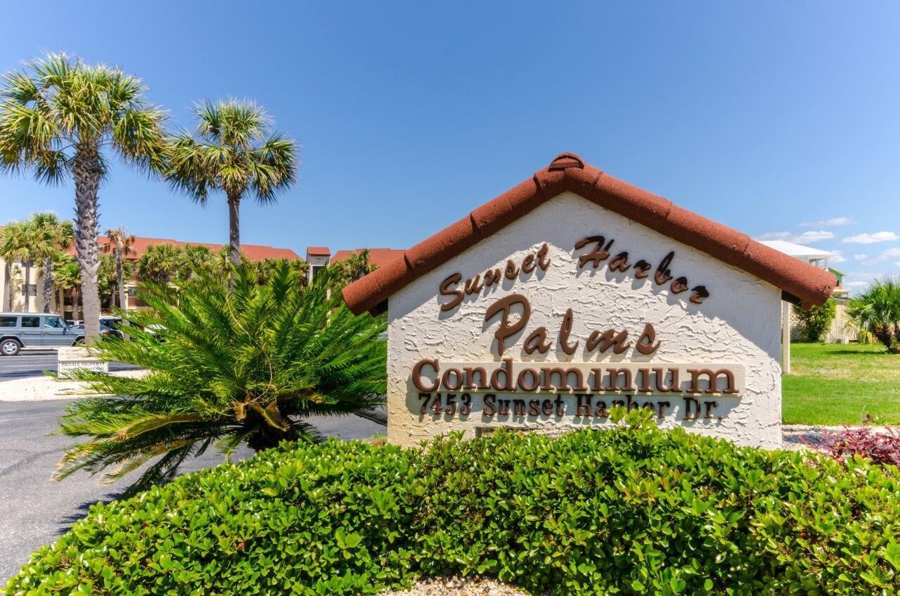 Schild für das Sunset Harbors Palm Condominium mit freiem Blick auf die umliegende Bepflanzung und Palmen.
