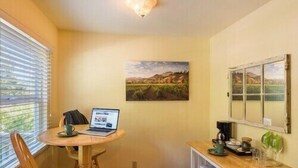 A small, cozy room with a round wooden table, a laptop, and a painting of a landscape on the wall. - Comfort and Style in Our Queen Cottage (Calistoga)