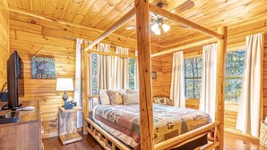 Una cama con dosel de madera con colcha, un televisor sobre una cómoda de madera, y un letrero que dice "LOOSE CREEK LODGE".