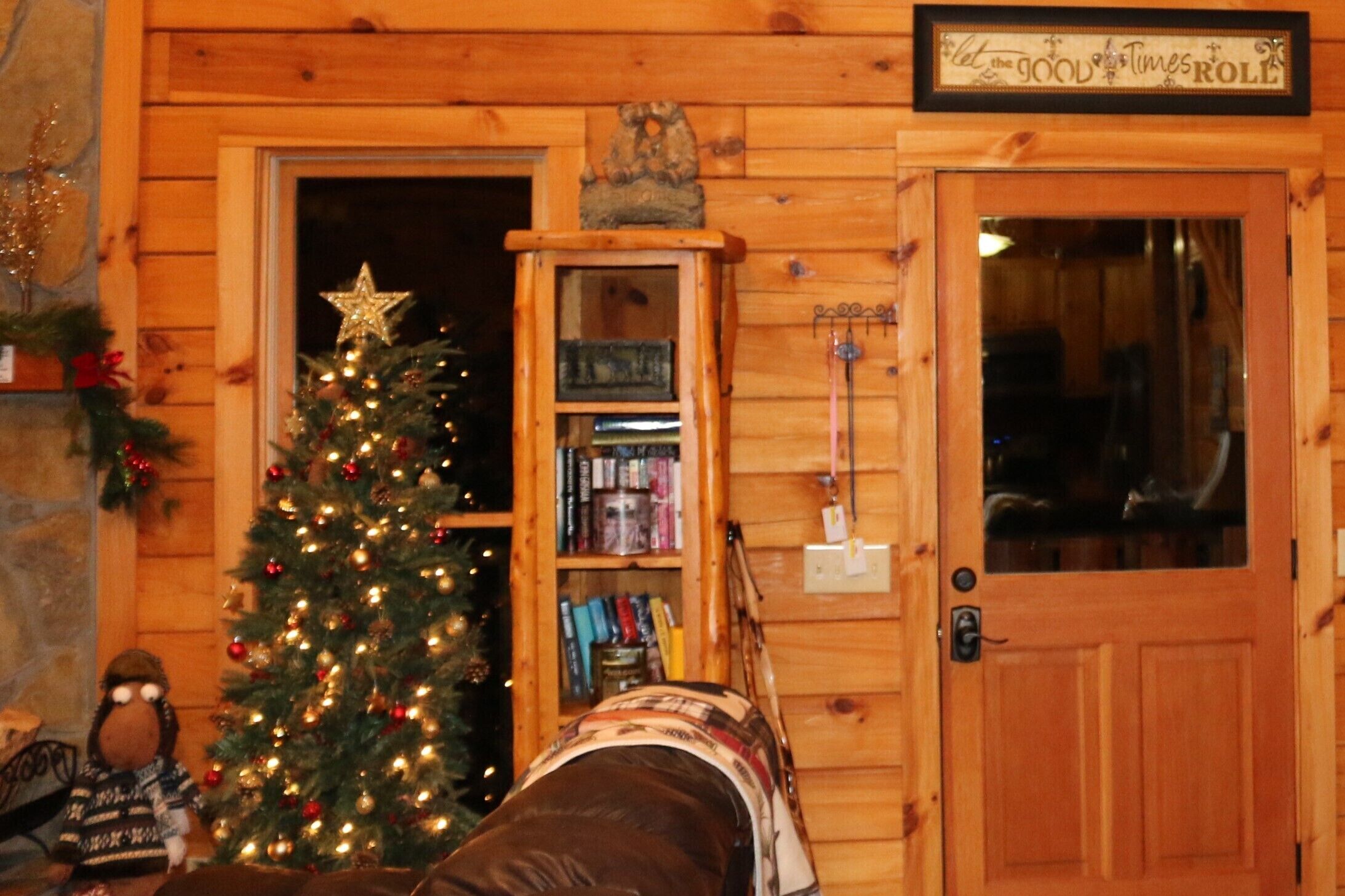 Quarto acolhedor com decoração em madeira, árvore de Natal, estante de livros e porta com uma placa em cima.