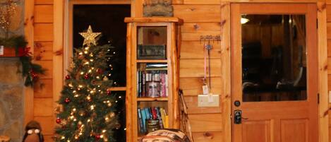 Quarto acolhedor com decoração em madeira, árvore de Natal, estante de livros e porta com uma placa em cima.