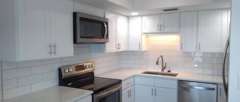 A modern kitchen with white cabinets, stainless steel appliances, and a tiled backsplash.