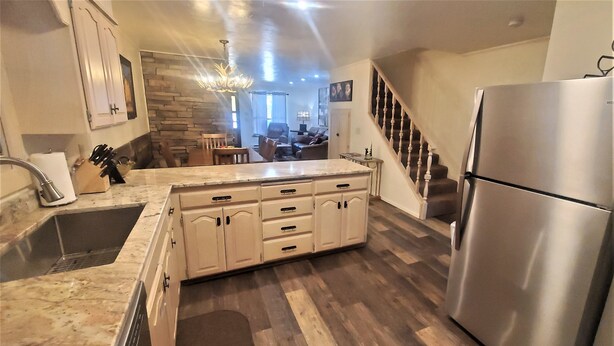 A kitchen with a marble countertop, wooden cabinets, a stainless steel refrigerator, and a wooden staircase.