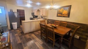 A compact kitchen with wooden cabinets, a dining table with chairs, a refrigerator, a microwave, and a sink.