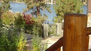 A wooden deck overlooking a lake with a fenced area and trees. - First-Tier Lakefront Log Charmer! Lakeview Spa In Gazebo,Fireplace,Deck,Sledding (Big Bear Lake)