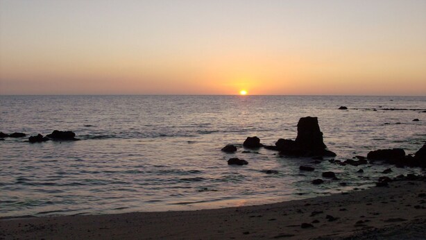 Un coucher de soleil sur une plage rocheuse aux eaux calmes.