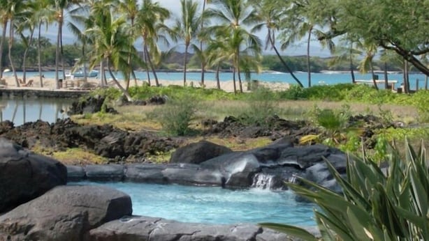 A tropical resort with a natural pool surrounded by rocks and palm trees.