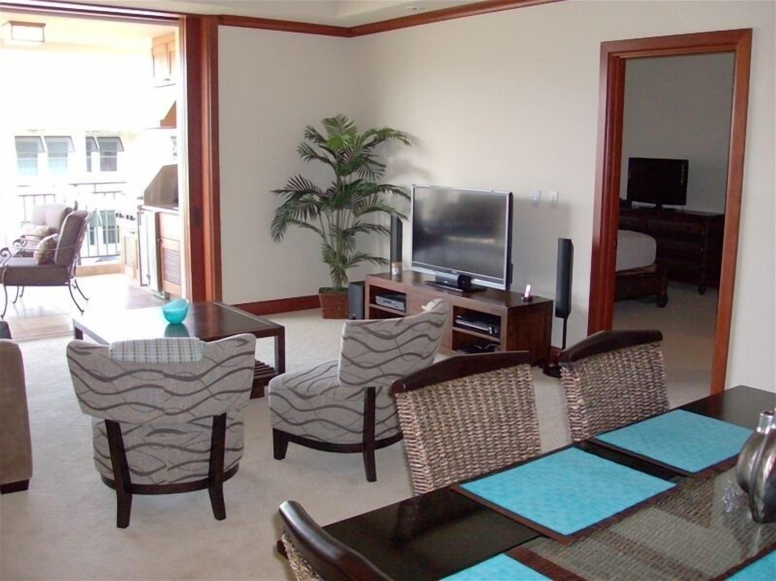A living room with a TV, a dining table with chairs, and a potted plant.