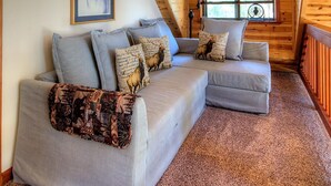 A cozy loft bedroom with a sloped ceiling, a large window with blinds, a sofa with patterned cushions, and a framed picture on the wall. - Mystic Views (Yosemite National Park)